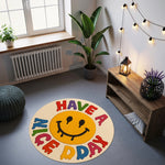 Ortası sarı smiley yüzlü, göz ve ağız kısmı akışkan boya damlama efektiyle tasarlanmış, çevresinde mavi, kırmızı, yeşil ve sarı tonlarda “HAVE A NICE DAY” yazısı yer alan, yuvarlak kesim, eğlenceli grafik halı tasarımı.
