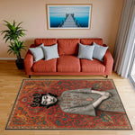 Gri zemin üzerinde zarif kadın silueti, çevresinde turuncu ve yeşil tonlarda stilize bitkisel süslemeler ve simetrik çerçeve bordürü bulunan modern-klasik tarz halı; illüstratif kompozisyon ve zengin motif yoğunluğu.
