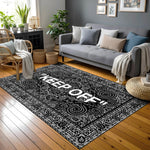 Siyah zemin üzerinde beyaz “KEEP OFF” tipografisi, etrafında yoğun paisley ve arabesk desenlerle çerçevelenmiş modern halı; yüksek kontrastlı siyah-beyaz renk paleti, simetrik bordür yapısı ve grafik odaklı çağdaş tasarım.
