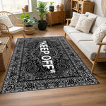 Ortada büyük tipografik yazı, çevresinde ince detaylı paisley ve floral desenlerden oluşan çerçeve bulunan siyah-beyaz halı; klasik süsleme dili ile modern grafik tasarımın birleştiği dikkat çekici yüzey kompozisyonu.
