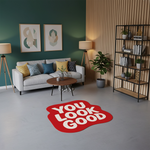 Grafik tasarım odaklı mesaj halısı; yuvarlak konturlu kırmızı form, merkezde büyük ve okunaklı beyaz “YOU LOOK GOOD” yazısı, pop art etkili, sade renk paleti ve güçlü tipografik vurgusuyla öne çıkan baskılı ürün.
