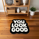 Minimal ve güçlü görünüme sahip tipografi halısı; siyah zemin üzerinde kalın, yuvarlak köşeli beyaz “YOU LOOK GOOD” yazısı, net kontrast sunan, modern pop kültür estetiğinde, figür kesim grafik baskı tasarımı.
